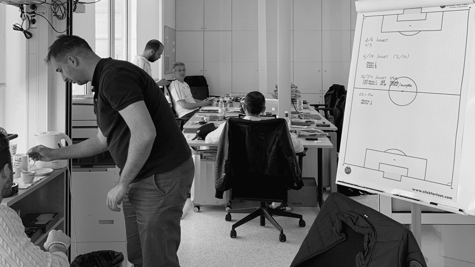 Coaching staff working at desks with a tactics easel in an office.